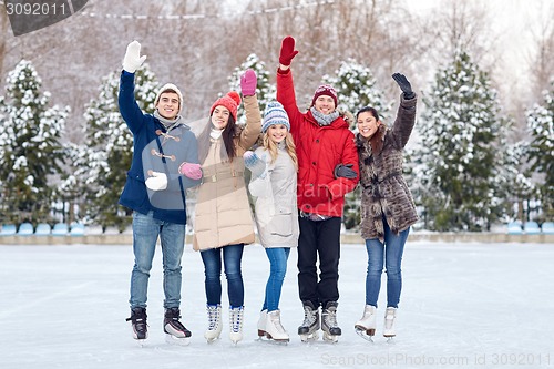 Image of happy friends ice skating on rink outdoors