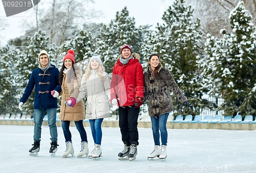 Image of happy friends ice skating on rink outdoors