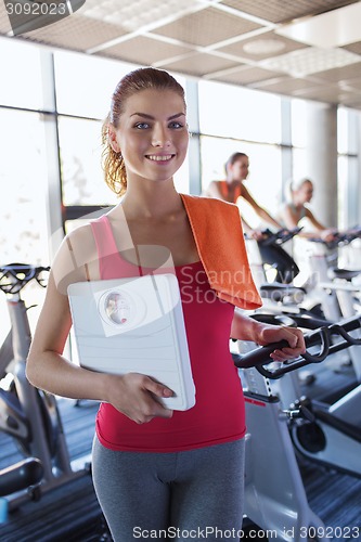 Image of smiling woman with scales and towel in gym