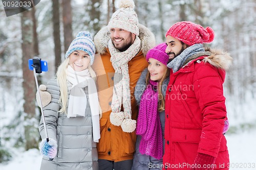 Image of smiling friends with smartphone in winter forest
