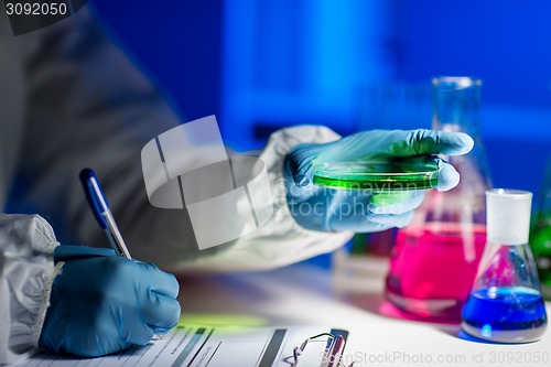 Image of close up of scientist writing test results in lab