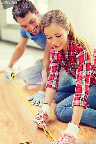 Image of smiling couple measuring wood flooring