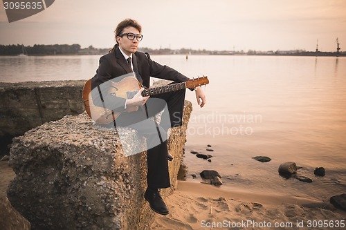 Image of Male musician and his guitar on shore