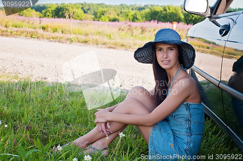 Image of Happy brunette woman sitting near car