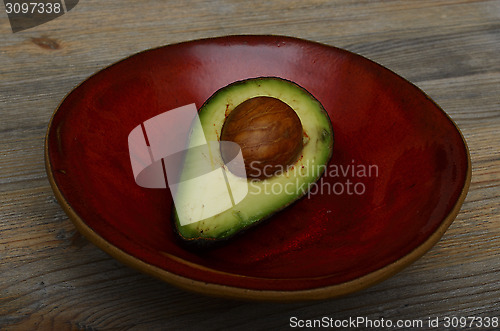 Image of avocado half on a red ceramic bowl