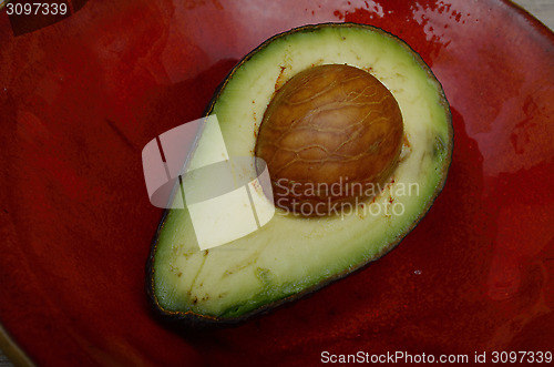Image of fresh avocado half on a red ceramic plate