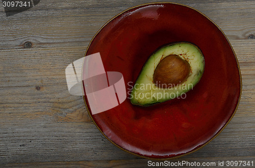Image of fresh avocado half on a red ceramic saucer