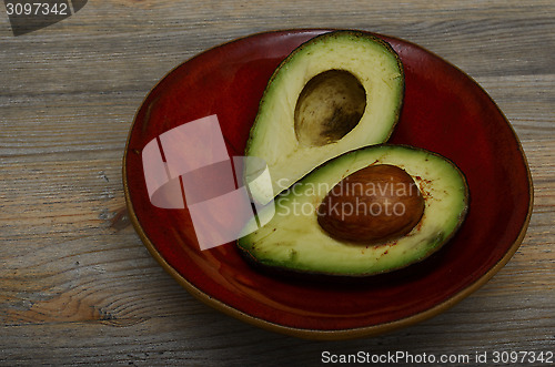 Image of two halves of avocado on red ceramic bowl