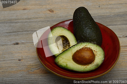 Image of whole avocado and two halves on a red ceramic saucer