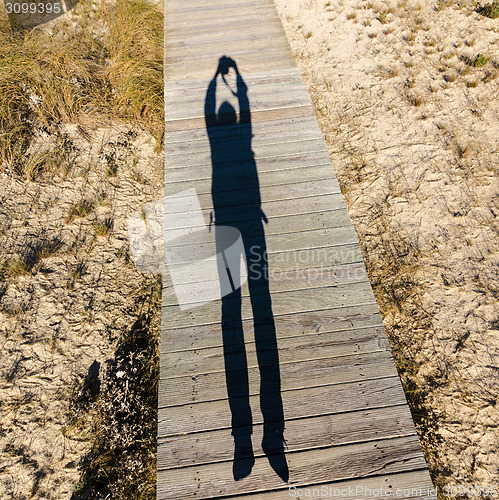 Image of Elongated Shadow Jumping Man on a Wooden Walkway