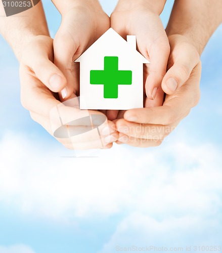 Image of hands holding paper house with green cross