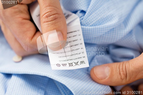 Image of close up of male hands holding shirt and label