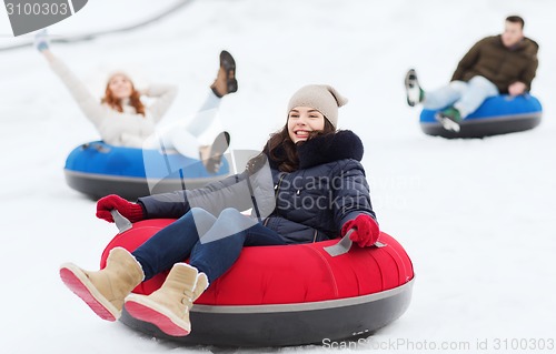 Image of group of happy friends sliding down on snow tubes