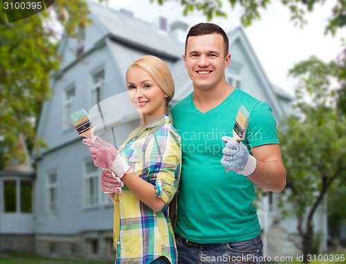 Image of smiling couple with paint brushes over house