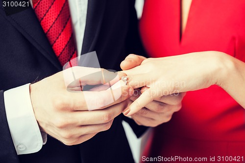 Image of man putting  wedding ring on woman hand