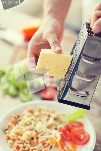 Image of close up of male hands grating cheese over pasta