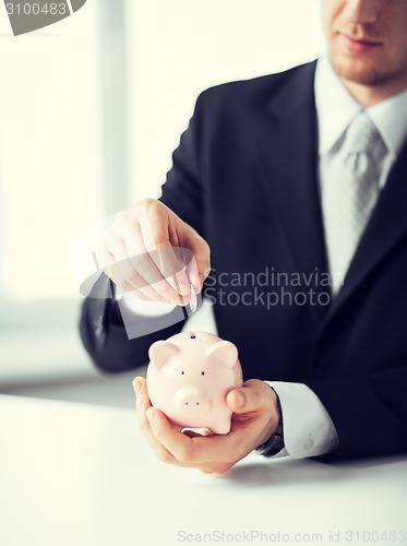 Image of man putting coin into small piggy bank