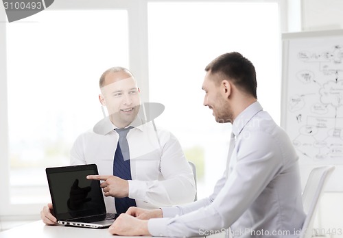 Image of two smiling businessmen with laptop in office