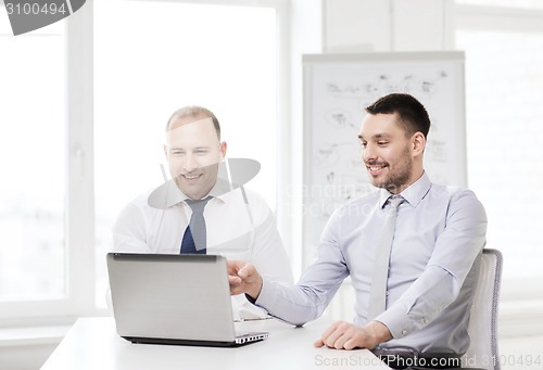 Image of two smiling businessmen with laptop in office