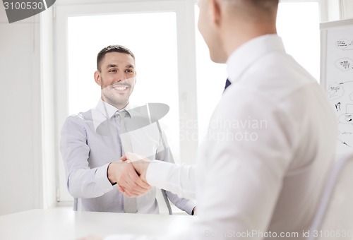 Image of two smiling businessmen shaking hands in office