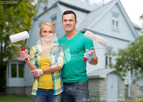 Image of smiling couple with paint rollers over house