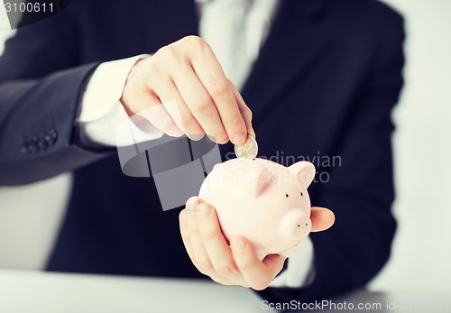 Image of man putting coin into small piggy bank