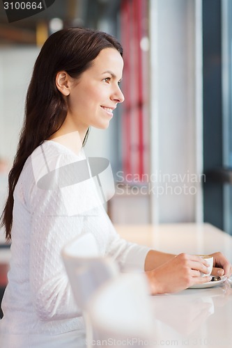 Image of smiling young woman drinking coffee at cafe