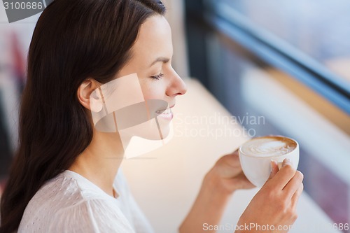 Image of smiling young woman drinking coffee at cafe