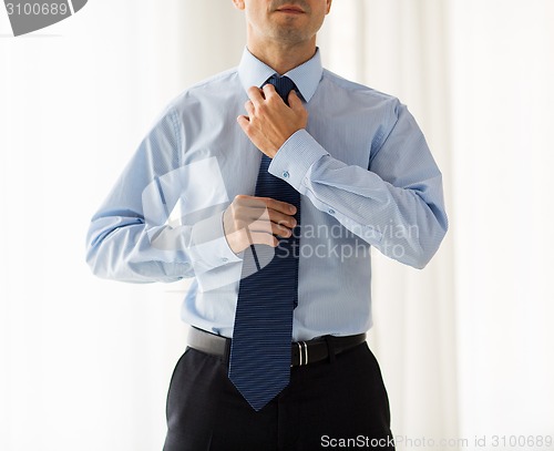 Image of close up of man in shirt adjusting tie on neck