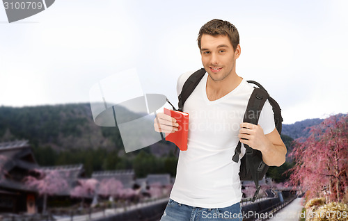 Image of happy young man with backpack and book travelling