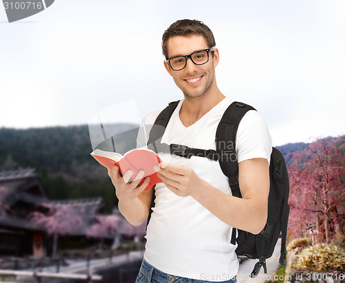 Image of happy young man with backpack and book travelling