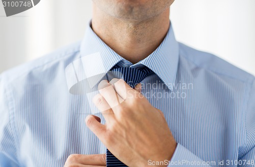 Image of close up of man in shirt adjusting tie on neck