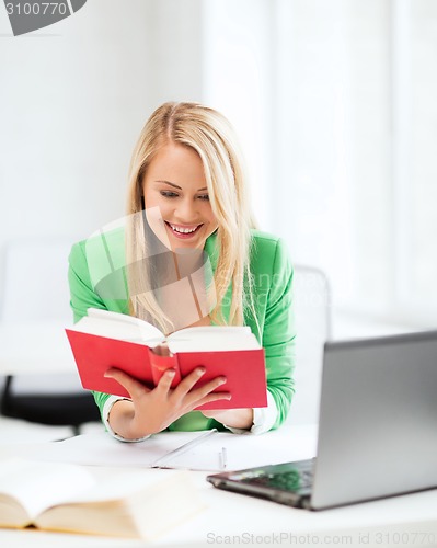 Image of smiling student girl reading book in college