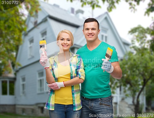 Image of smiling couple with paint brushes over house