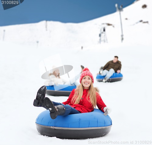 Image of group of happy friends sliding down on snow tubes