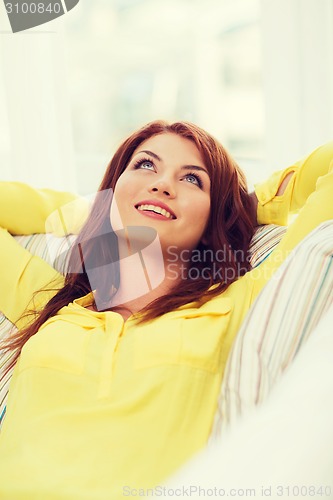 Image of smiling young woman lying on sofa at home