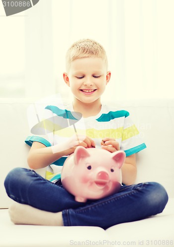 Image of smiling little boy with piggy bank at home