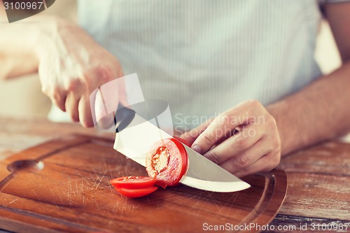 Image of male hand cutting tomato on board with knife