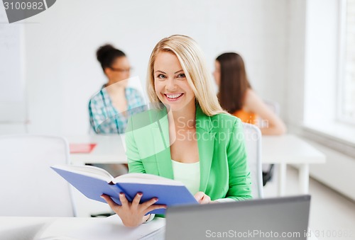 Image of smiling young girl reading book at school