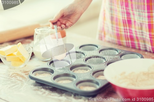 Image of close up of hand filling muffins molds with dough