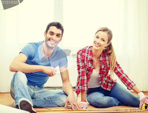 Image of smiling couple measuring wood flooring