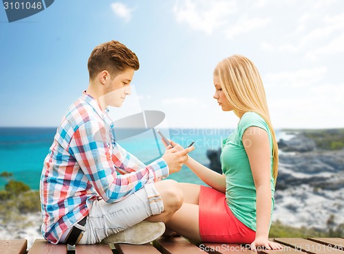 Image of couple with smartphones sitting on bench