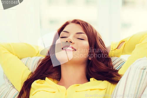 Image of smiling young woman lying on sofa at home