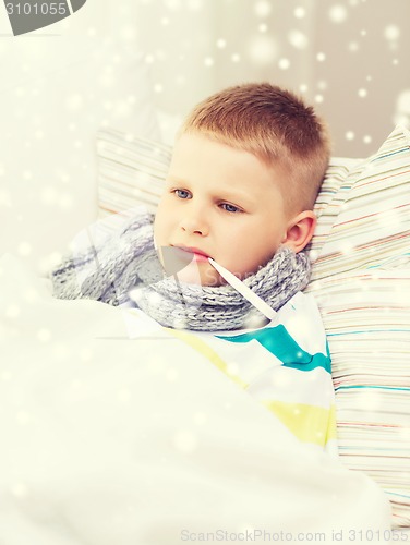 Image of ill boy with thermometer lying in bed at home