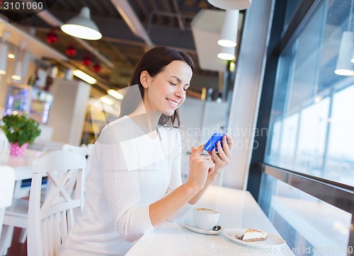 Image of smiling woman with smartphone and coffee at cafe