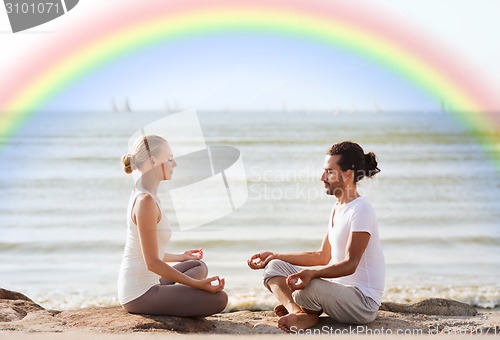 Image of happy couple meditating in lotus pose on beach