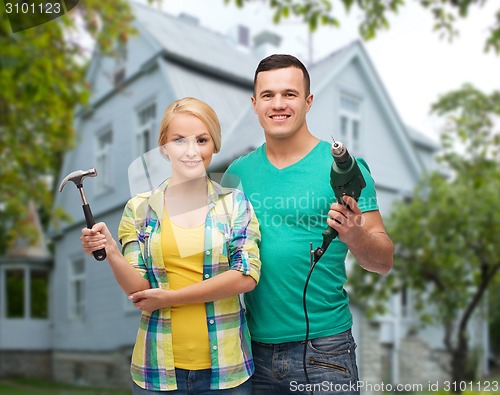 Image of smiling couple with hammer and drill over house