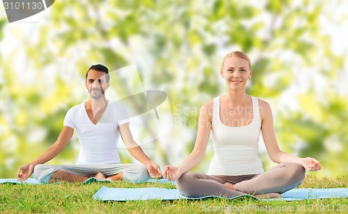 Image of smiling couple making yoga exercises outdoors