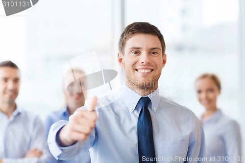 Image of smiling businessman showing thumbs up in office