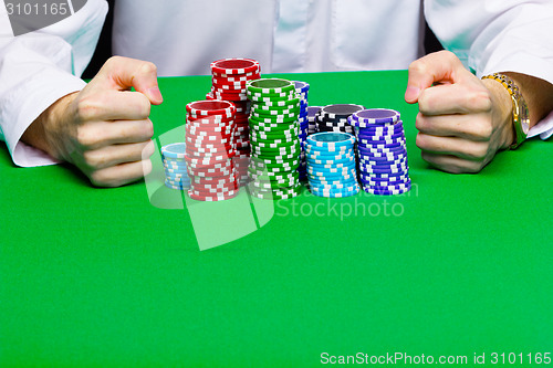 Image of Man with a bunch of chips. Green table